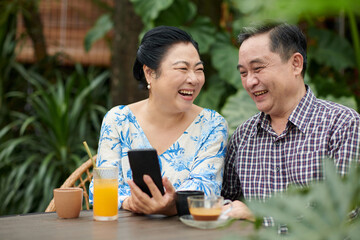 Senior Vietnamese couple laughing at post on social media