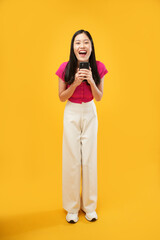 This portrait is of a young Asian woman wearing a pink t-shirt, screaming and holding a mobile phone in hand, Isolated on a yellow background.
