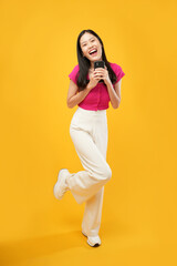 Fototapeta na wymiar This portrait is of a young Asian woman wearing a pink t-shirt, holding a modern cellular to check messages with a curious happy expression. Isolated on a yellow background.