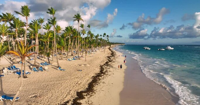 Tropical beach, caribbean sea and walking people on the sandy shore welcoming ocean sunrise over Punta Cana, Dominican Republic, aerial landscape