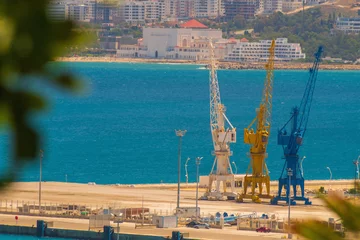 Foto op Plexiglas Harbour cranes against the background of the blue sea with slightly blurred contours due to the heat and warm air currents in the air. Concept of cargo transportation by sea © Po