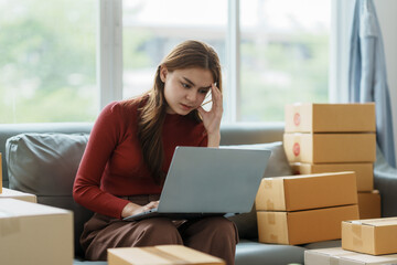 Young woman working at small business ecommerce using laptop stressed and frustrated surprised and angry face. Small online business owner woman stressed headache with parcel box at home.