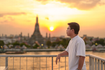 tourist man enjoys view to Wat Arun Temple in sunset, Traveler visits Temple of Dawn near Chao...