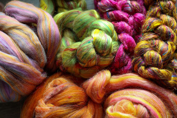 Closeup detail of colourful sheep wool merino, alpaca and silk fibres in a roving pleat, ready for spinning on traditional spinning wheel.	