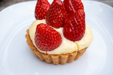 Small tart with strawberries and cream on white plate in cafe
