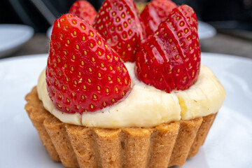 Small tart with strawberries and cream on white plate in cafe

