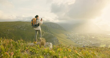 Woman, hiking and video recording on mountains in adventure, wellness and health with nature and cityscape. Person with backpack and trekking photography on green hill, travel or eco friendly journey - Powered by Adobe