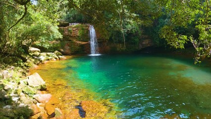 Jungle waterfall with white waters running down Rocky ridge of hill to blue green water of lagoon or pool. Sun rays passing through clear water. Rangshokham falls of Meghalaya.