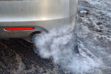 Car exhaust pipe smoking in cold weather. Engine warming up at idle in winter season. Smoke from...