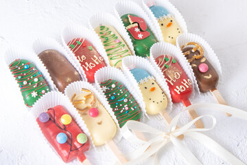 Christmas dessert. Sweet food. Cheesecake on a stick in the shape of ice cream. Children's treat in winter. Candy Christmas tree, snowman, deer and Santa Claus. Gingerbread cookies background.