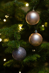Close-up of Christmas balls hanging on a tree with Christmas lights in the background. 