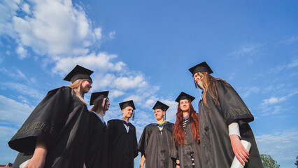 Graduating students stand in a semicircle on a sunny summer afternoon.
