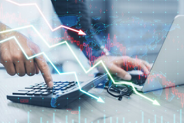 Close up of businessman hands using laptop and calculator on desk with falling forex chart arrows...