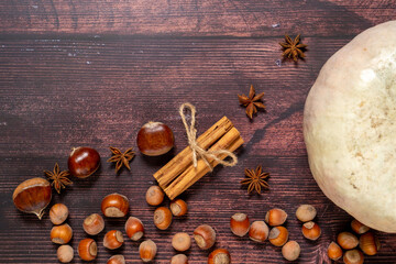 Autumn flatlay with pumpkin, chestnuts, star anise, cinnamon and cobnuts on a brown wooden...