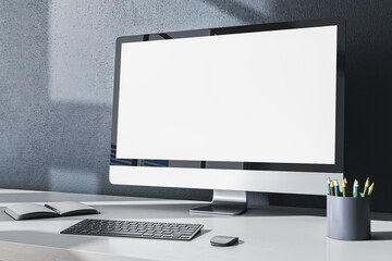 Fototapeta premium Contemporary designer office desktop with empty white mock up computer monitor, supplies and other items on gray wall background. 3D Rendering.
