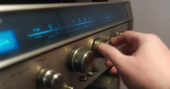 Close-up of a hand turning a knob to change frequency on a retro radio with metal design and blue backlit display