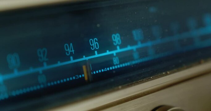 Close-up of a moving pointer on a blue backlit scale with radio freventions. Vintage radio tuning