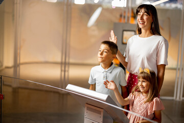 Mom with kids are excited to interact with a robot, visiting together science museum. Concept of...