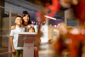 Mom with kids are excited to interact with a robot, visiting together science museum. Concept of...