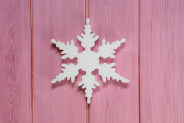 One white snowflake on a wooden pink table. New years decoration flatlay
