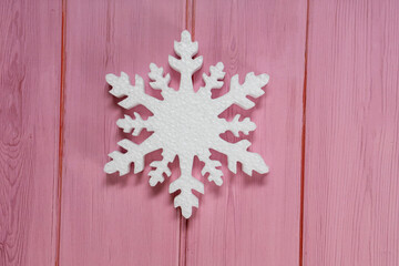 One white snowflake on a wooden pink table. New years decoration flatlay