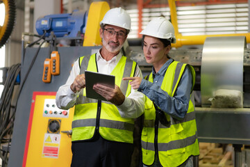 Senior manager train female technician working in metalwork production factory. Industrial engineer teamwork standing in manufacturing facility talking machinery maintenance in heavy steel industry.