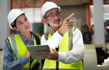 Senior manager train female technician working in metalwork production factory. Industrial engineer teamwork standing in manufacturing facility talking machinery maintenance in heavy steel industry.