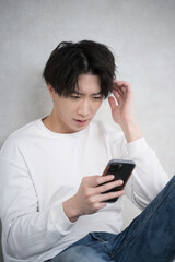 Handsome man holding a phone with a troubled or negative expression leaning against a wall.