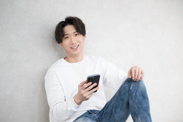 壁に寄りかかりスマホを持つハンサムな男性 カメラ目線