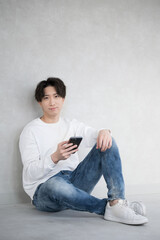 壁に寄りかかりスマホを持つハンサムな男性 カメラ目線 縦