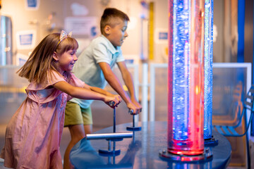 Little kids pump a bubbles into tubes studying physical phenomena in an interactive way, visiting together science museum - obrazy, fototapety, plakaty