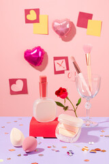 Heart balloons and decorative paper are stuck on the pink wall. Lipstick, cushion boxes, makeup brushes and makeup sponges are displayed on the table.
