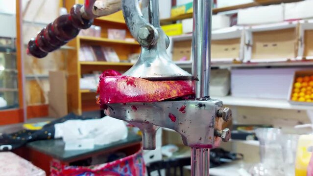 Piece of pomegranate lies in a hand press juicer. Making a fruit drink smoothie in juice extractor at a local cheap cafe in Egypt, untidy dirty work area. Close up
