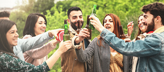 Group of jovial young adults toasting with beer bottles, celebrating together in a park.