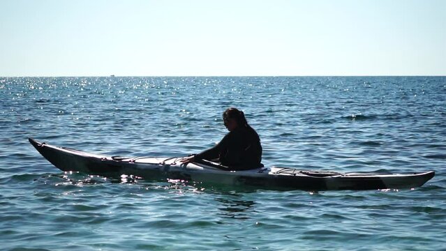 Woman sea kayak. Happy smiling woman in kayak on ocean, paddling with wooden oar. Calm sea water and horizon in background. Active lifestyle at sea. Summer vacation.