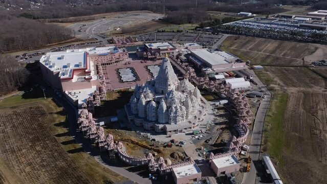 An aerial view of the Shri Swaminarayan Mandir in Robbinsville Twp, NJ on a sunny day, closed for the day. The camera tilted downwards, truck left and pan right orbiting the huge temple clockwise.
