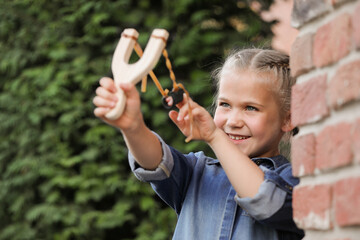 Little girl playing with slingshot outdoors. Kid's toy