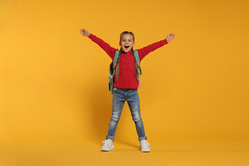 Fototapeta na wymiar Emotional schoolgirl with backpack on orange background