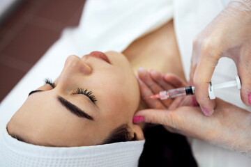 Beauty injections. Female cosmetologist in transparent gloves makes an injection in the lower jaw of her client.