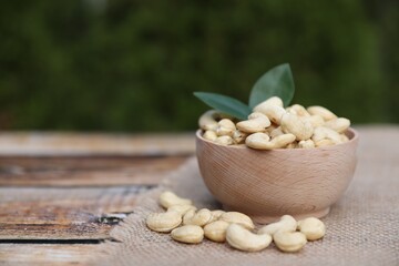 Fototapeta na wymiar Tasty cashew nuts in bowl on wooden table outdoors, space for text