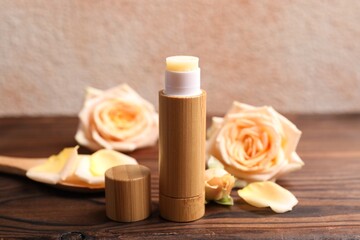Lip balm and rose flowers on wooden table, closeup