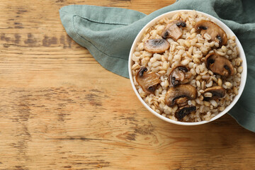 Delicious pearl barley with mushrooms in bowl on wooden table, top view. Space for text