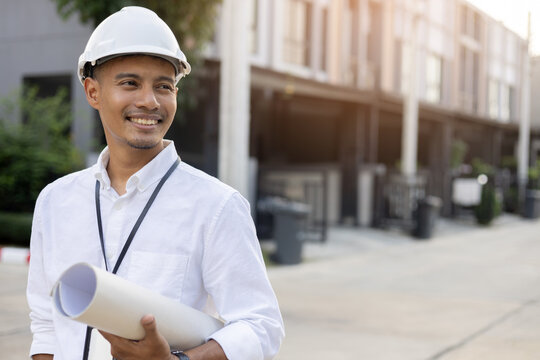 Close Up Indian Engineer Man Smile And Hold Blueprint Of Building Project In Front Of Site For Civil And Construction Concept