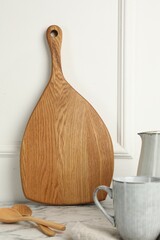 Wooden cutting board, spoons and dishware on white marble table
