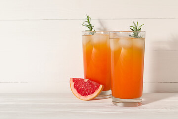 Tasty grapefruit drink with ice and rosemary in glasses on white wooden table. Space for text