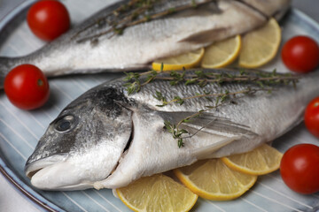 Raw dorado fish with thyme, lemon slices and tomatoes on table, closeup