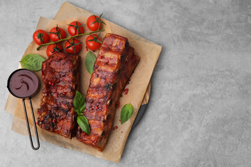 Tasty roasted pork ribs served with sauce, basil and tomatoes on grey table, top view. Space for text