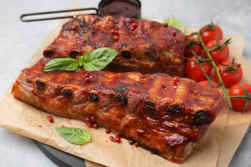 Tasty roasted pork ribs served with sauce, basil and tomatoes on grey table, closeup