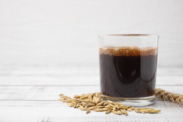 Cup of barley coffee, grains and spike on white wooden table, closeup. Space for text