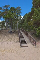 Fototapeta na wymiar Wooden stairs to sandy beach in autumn with clouds in sky, Lappohja, Finland.